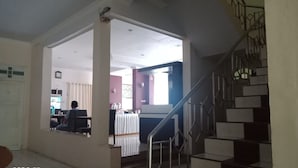 A room with a staircase, a table with chairs, and a person sitting at a table. - Hotel Monika (Rantepao)
