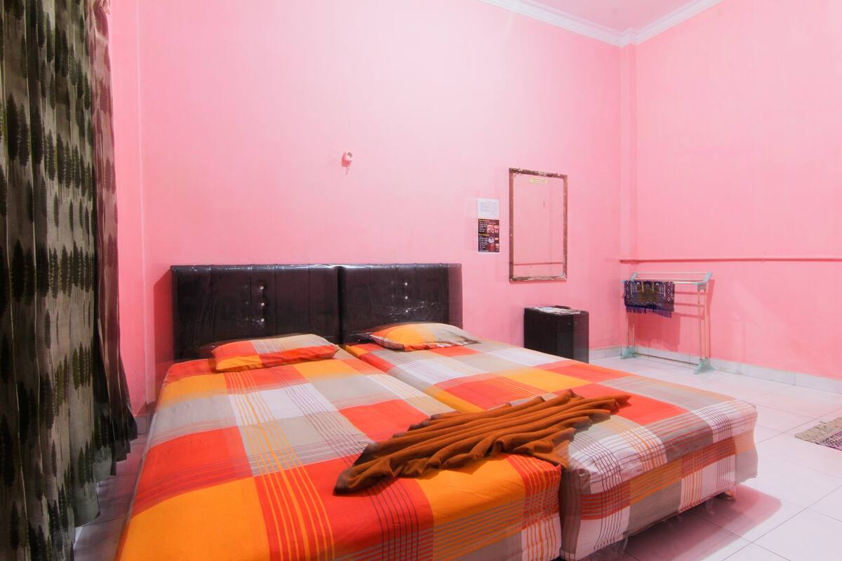 A room with pink walls, a bed with a checkered bedspread, a headboard, a bedside table, and a small shelf with items.