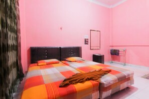 Una habitación con paredes rosas, una cama con colcha a cuadros, cabecero, mesita de noche y un estante con objetos.