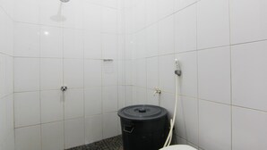 Un baño pequeño con azulejos, un inodoro, un cubo de basura negro y un cabezal de ducha.