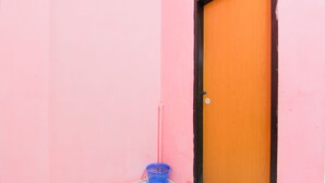 Una pared rosa con una puerta de madera y una cesta de plástico azul en el suelo.