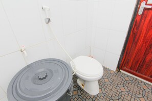 Un baño con inodoro, un cesto gris grande y una puerta roja.