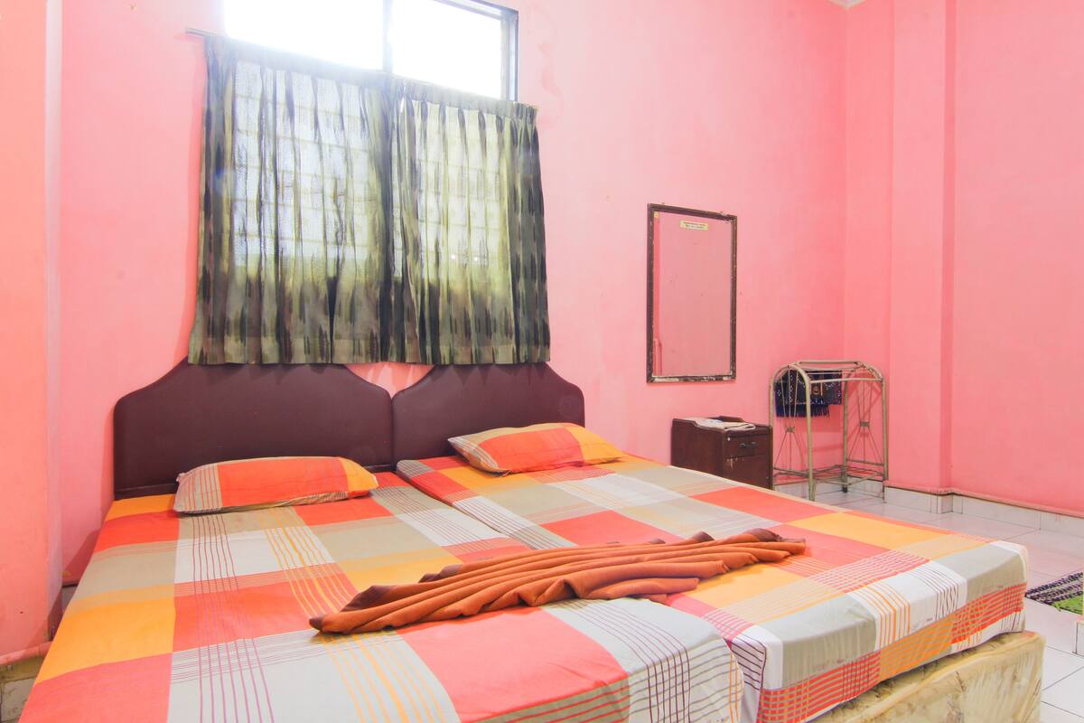 A bedroom with a large bed, pink walls, and a window with curtains.