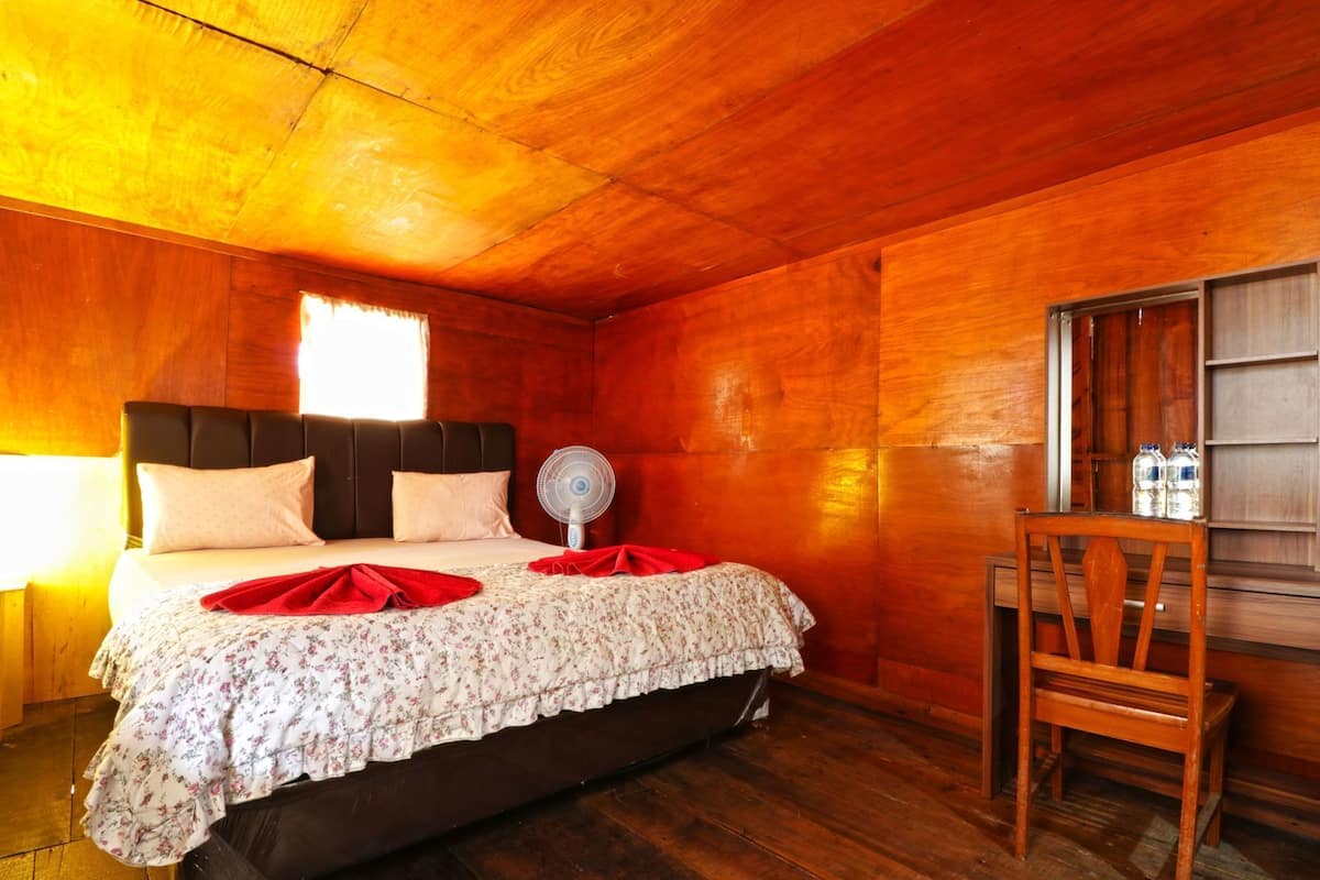 Quarto de madeira com uma cama, um ventilador e uma cadeira.