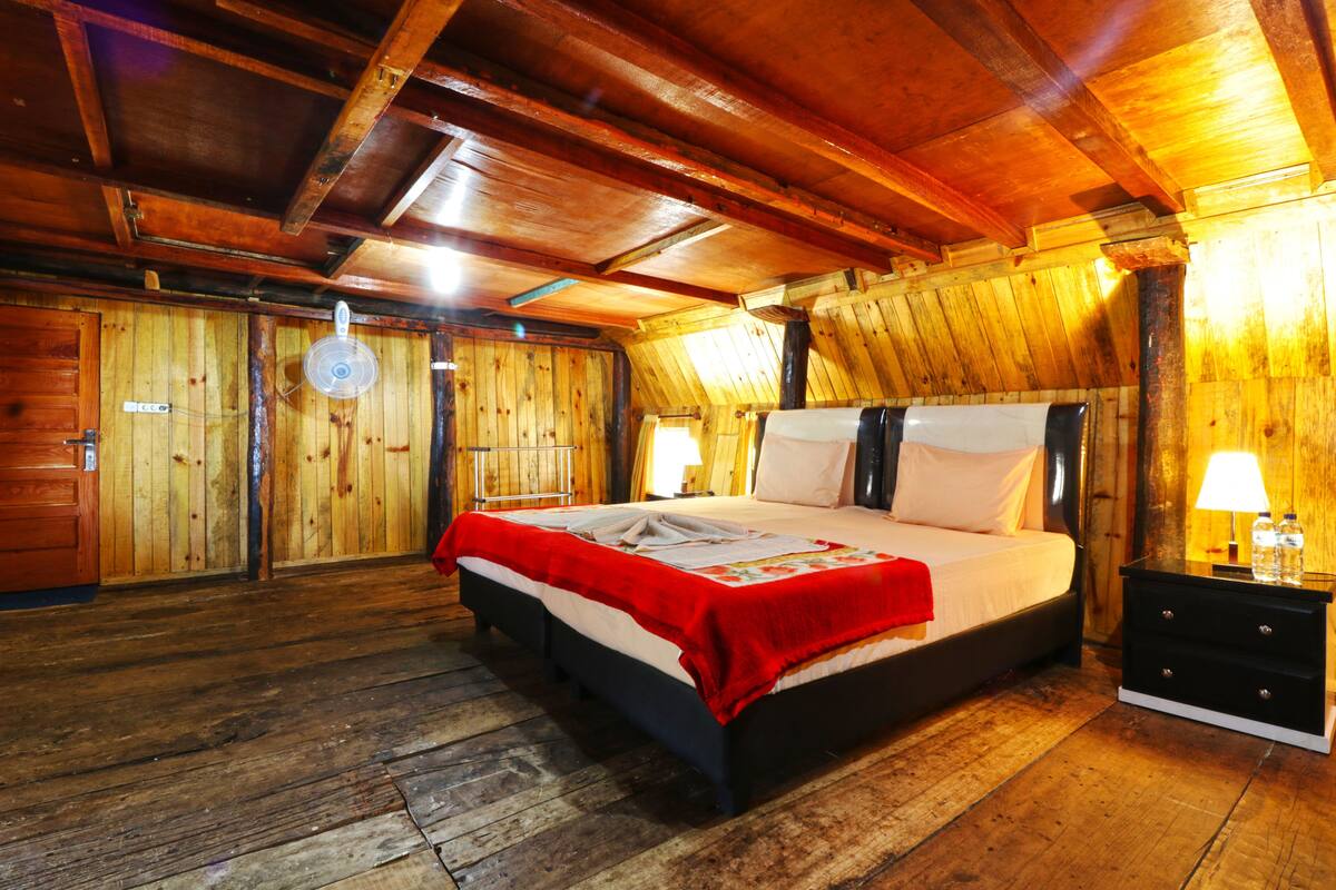 Quarto de madeira com cama, mesas de cabeceira e ventilador de teto.