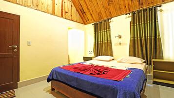 A bedroom with a wooden ceiling, a bed with a blue bedspread and red towels, a nightstand, and a wooden bench.
