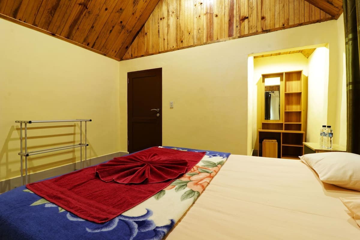 Quarto com teto de madeira, cama com toalha vermelha, suporte de metal e guarda-roupa de madeira com espelho.