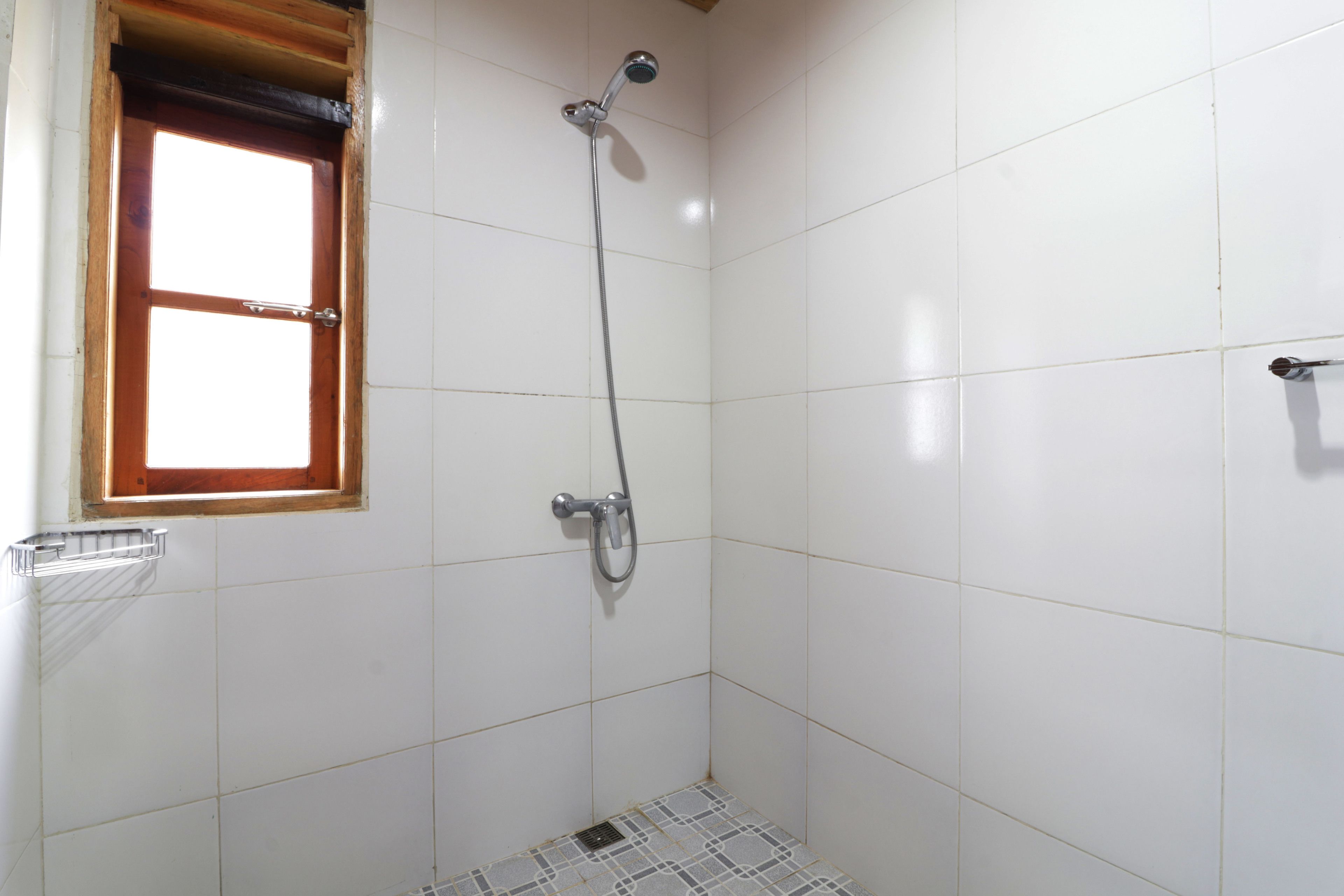 Un baño pequeño con azulejos, ducha, ventana y un perchero para toallas.