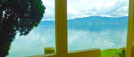 Ein Zimmer mit Seeblick und Blick auf Berge. Ein Sessel und ein kleiner Tisch sind vorhanden.