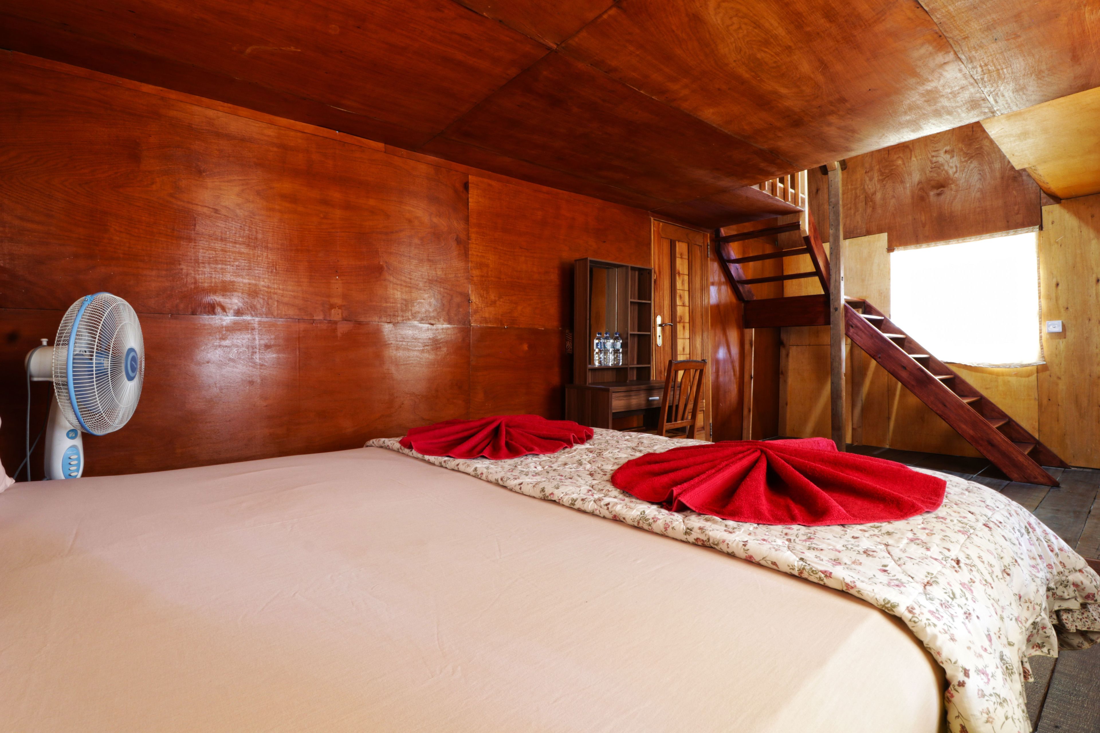 Una habitación de madera con una cama, un ventilador y una escalera.