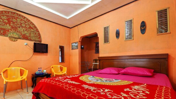 A room with a bed, two chairs, a TV, and a decorative wall piece. - Bangkit Nan Jaya (Berastagi)
