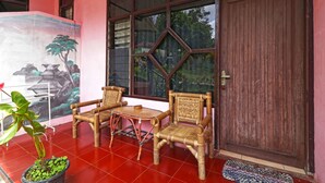 A room with two wicker chairs and a small table, a large window with a view of greenery, and a red tiled floor. - Bangkit Nan Jaya (Berastagi)