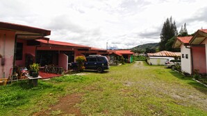 A residential area with houses, a dirt path, and parked cars. - Bangkit Nan Jaya (Berastagi)