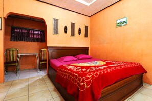 A bedroom with a wooden bed, a red bedspread, a small table, two chairs, and a window with curtains.