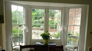 Une pièce avec une baie vitrée, une table à manger, deux chaises, une plante en pot et une lampe.