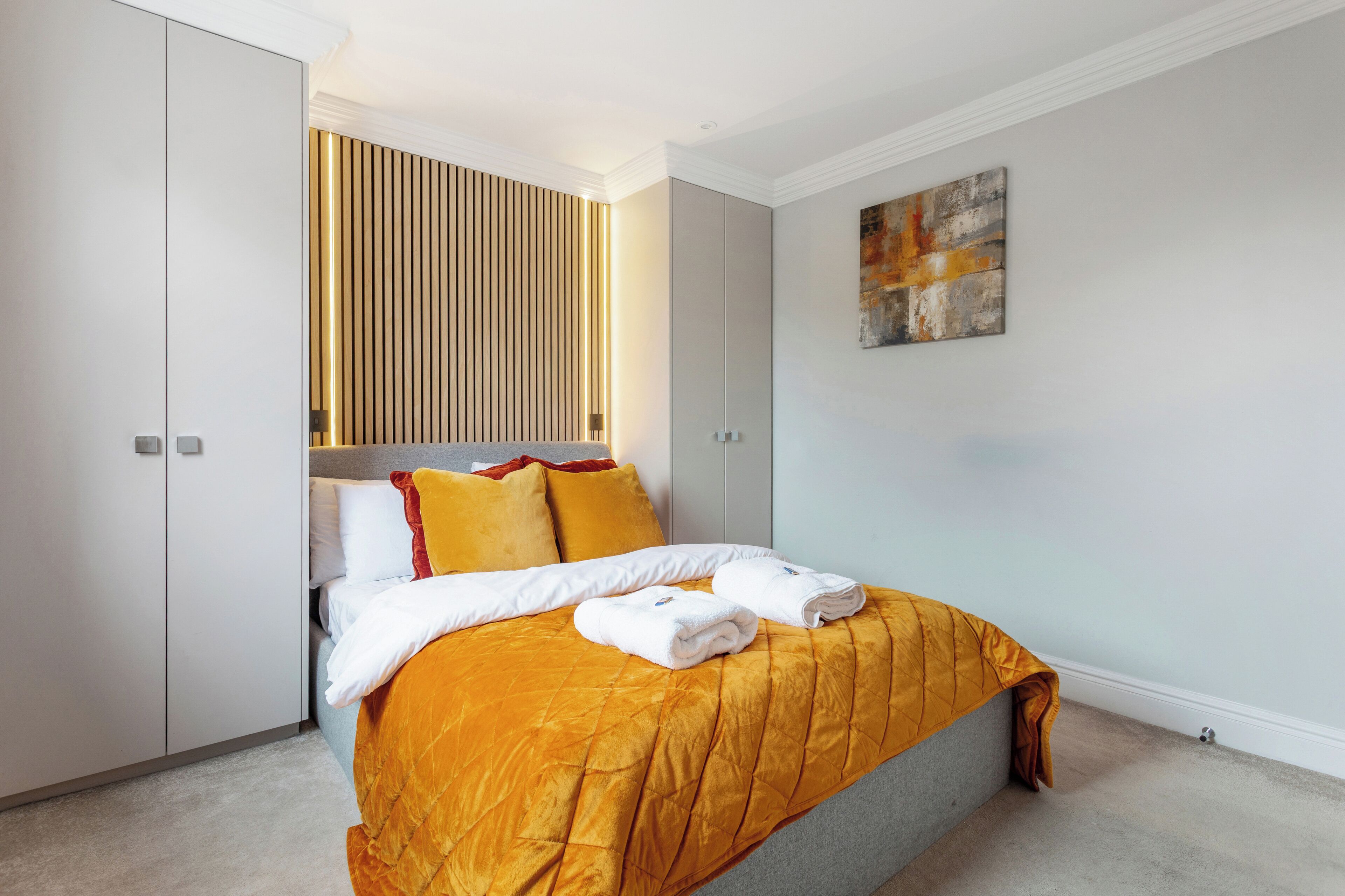 A modern hotel room with a large bed, a wardrobe, and a wall-mounted light panel.