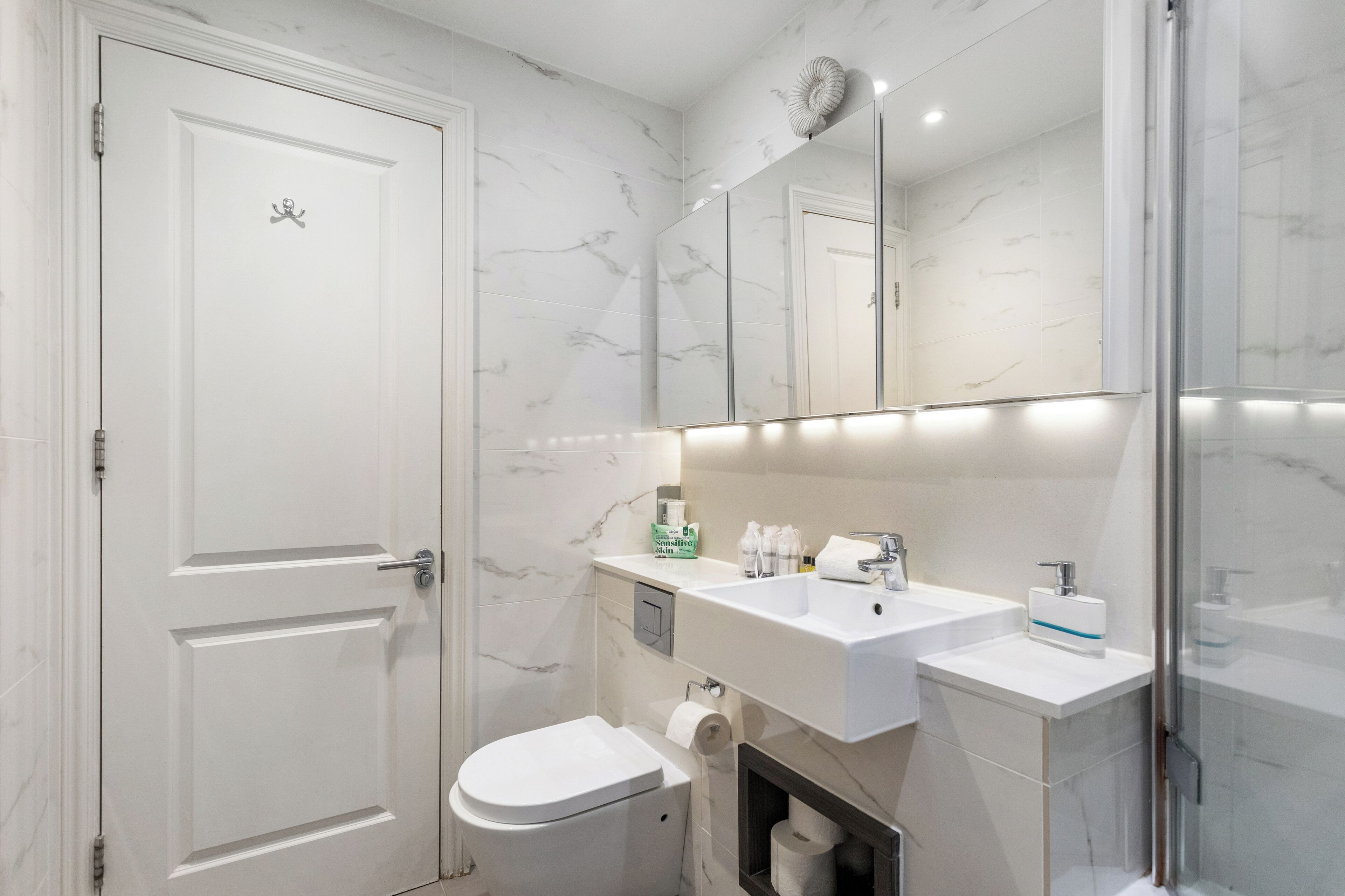 Un baño moderno con inodoro blanco, lavamanos y espejo.