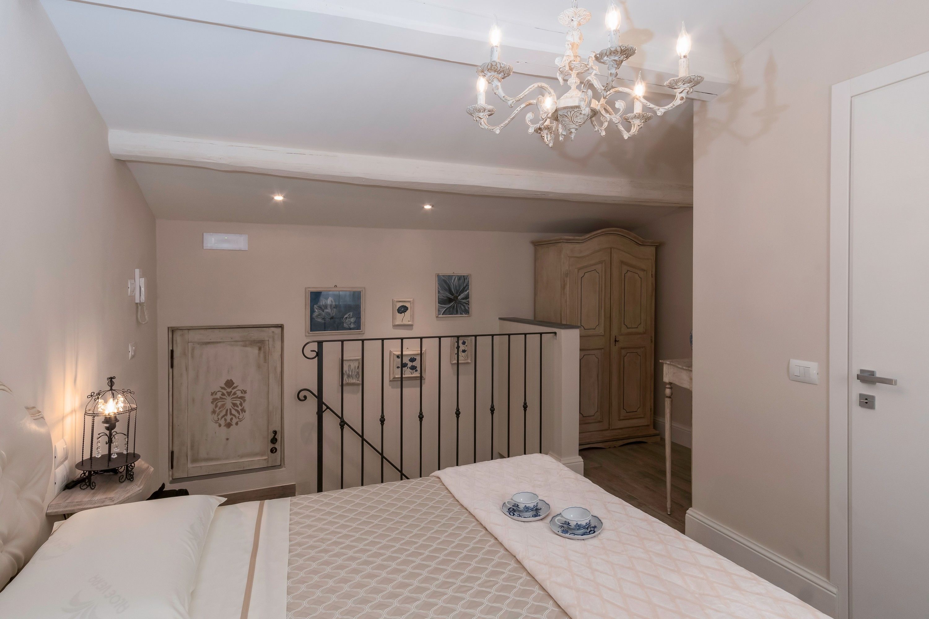 A bedroom with a bed, a chandelier, a wardrobe, and a door.