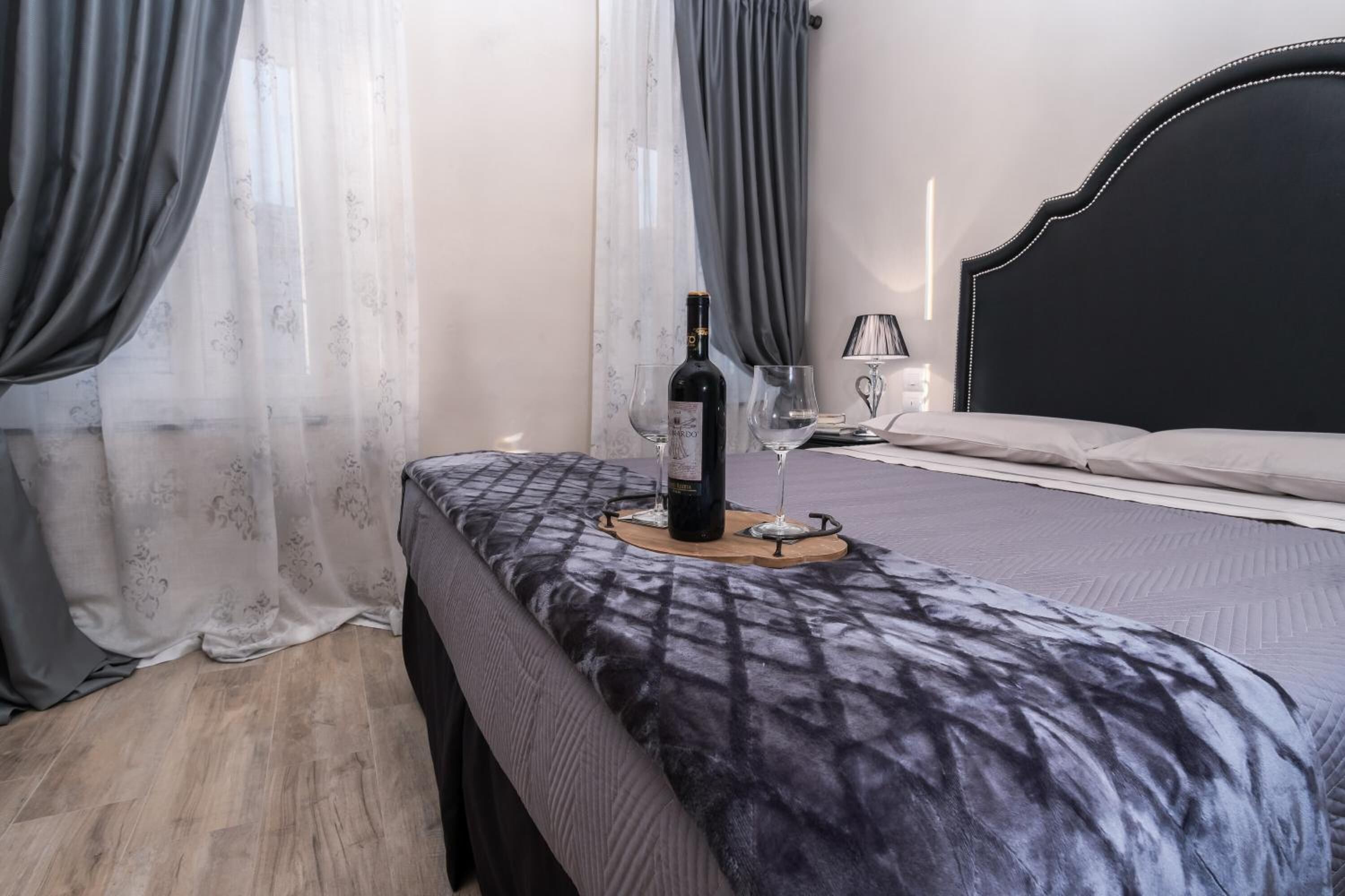 Une chambre à coucher avec un lit, une table de chevet sur laquelle se trouvent une bouteille et des verres, et des rideaux.
