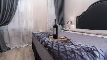 Une chambre à coucher avec un lit, une table de chevet sur laquelle se trouvent une bouteille et des verres, et des rideaux.