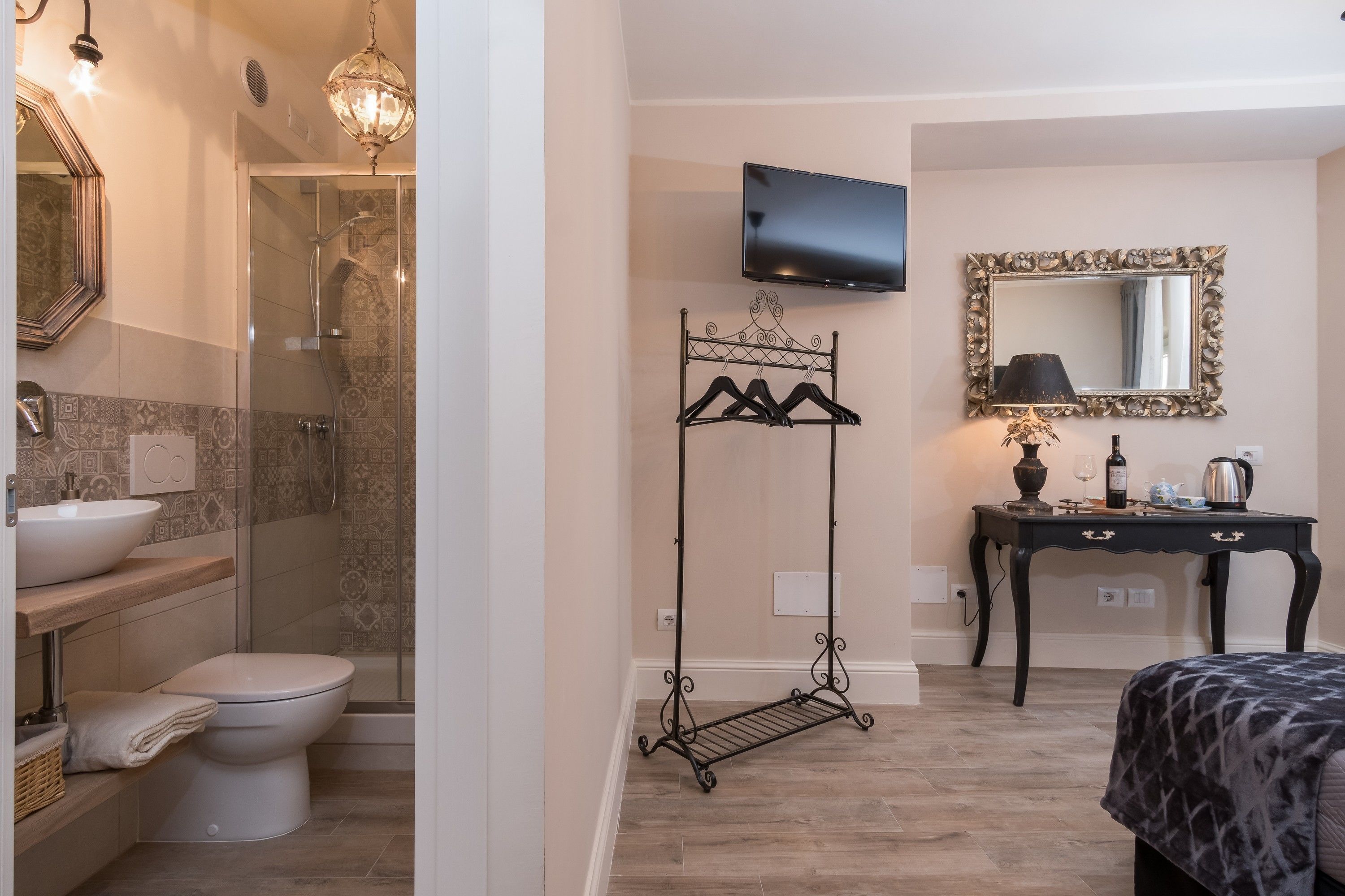 A modern bathroom with a shower, toilet, and sink. There is a TV mounted on the wall and a small table with a lamp.