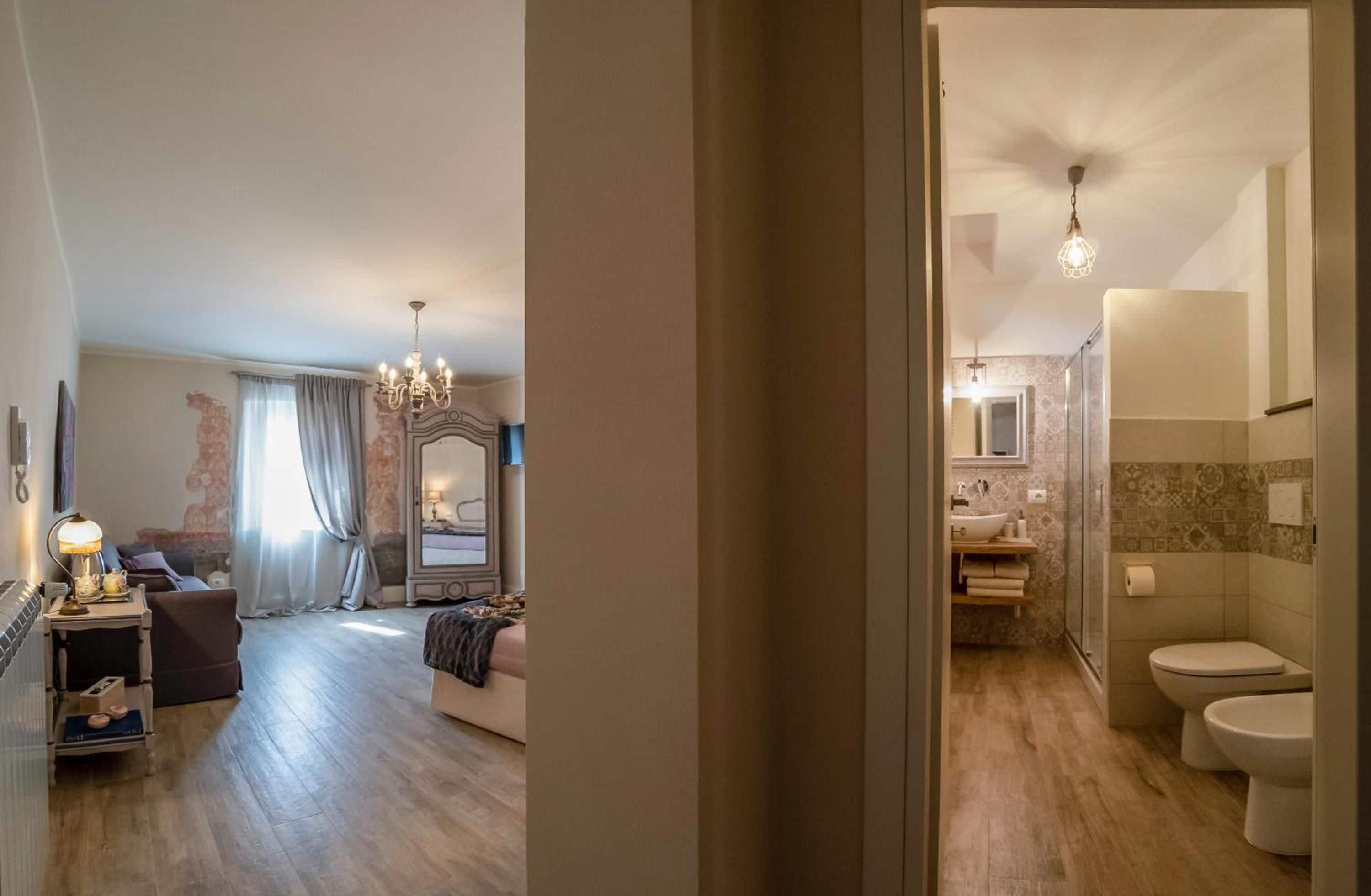 A hotel room with a sitting area, a bed, a chandelier, and a bathroom with a toilet and shower.