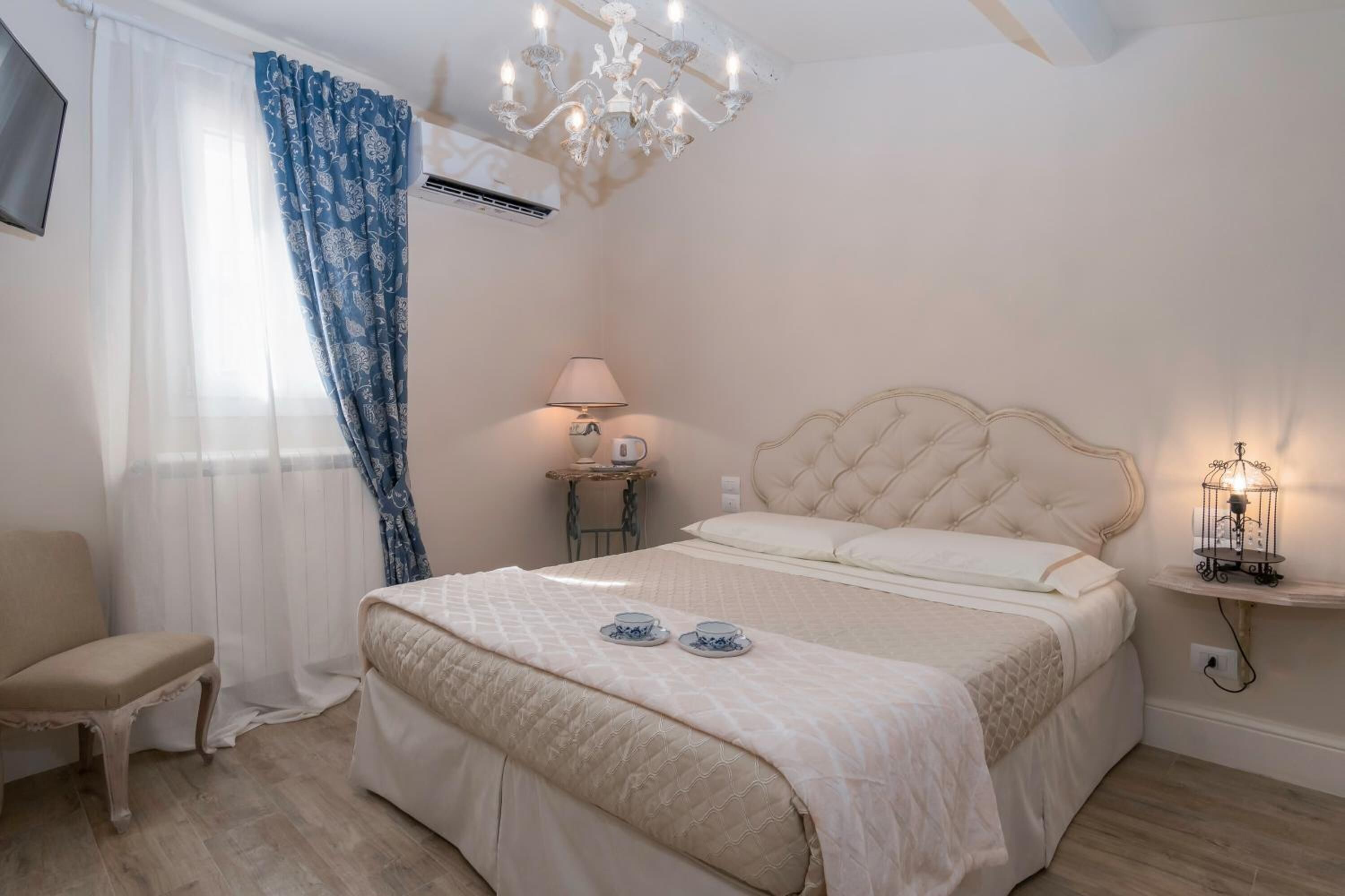 A bedroom with a bed, a chair, a bedside table with a lamp, and a decorative light fixture.