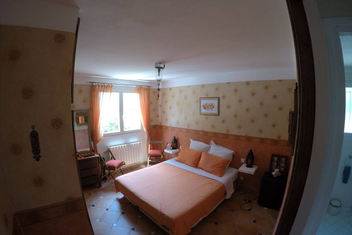 Un dormitorio con una cama, una silla, una mesita de noche, un radiador y una ventana con cortinas.