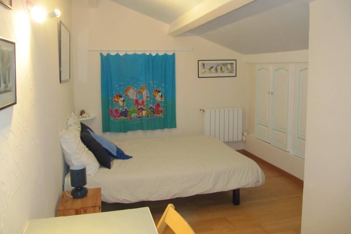 Un dormitorio con cama, una mesa, una silla, un radiador y una ventana con cortinas.