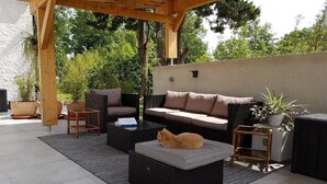Un patio al aire libre con mobiliario de mimbre, un banco acolchado y un gato.