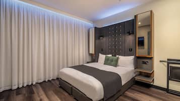 A modern hotel room with a large bed, a nightstand, a mirror, and a window with curtains.