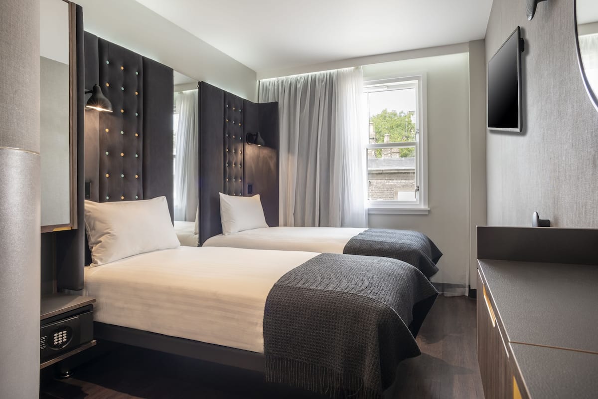 Hotellihuone, jossa on kaksi sänkyä, taulutelevisio, ikkuna verhoilla ja työpöytä lampulla.