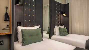 A hotel room with two beds, a mirror, a hanging bag, and a wall-mounted lamp.