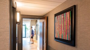 Un pasillo con una obra de arte colorida enmarcada en la pared, una puerta con una lámpara y suelo de madera.