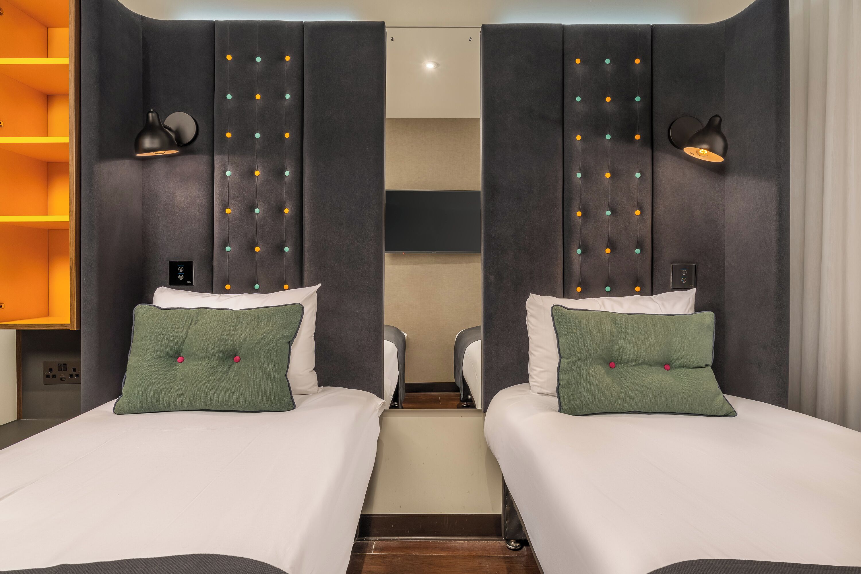 Ein Hotelzimmer mit zwei Betten, einem Schlafsofa, einem Fernseher und einer Wandleuchte.