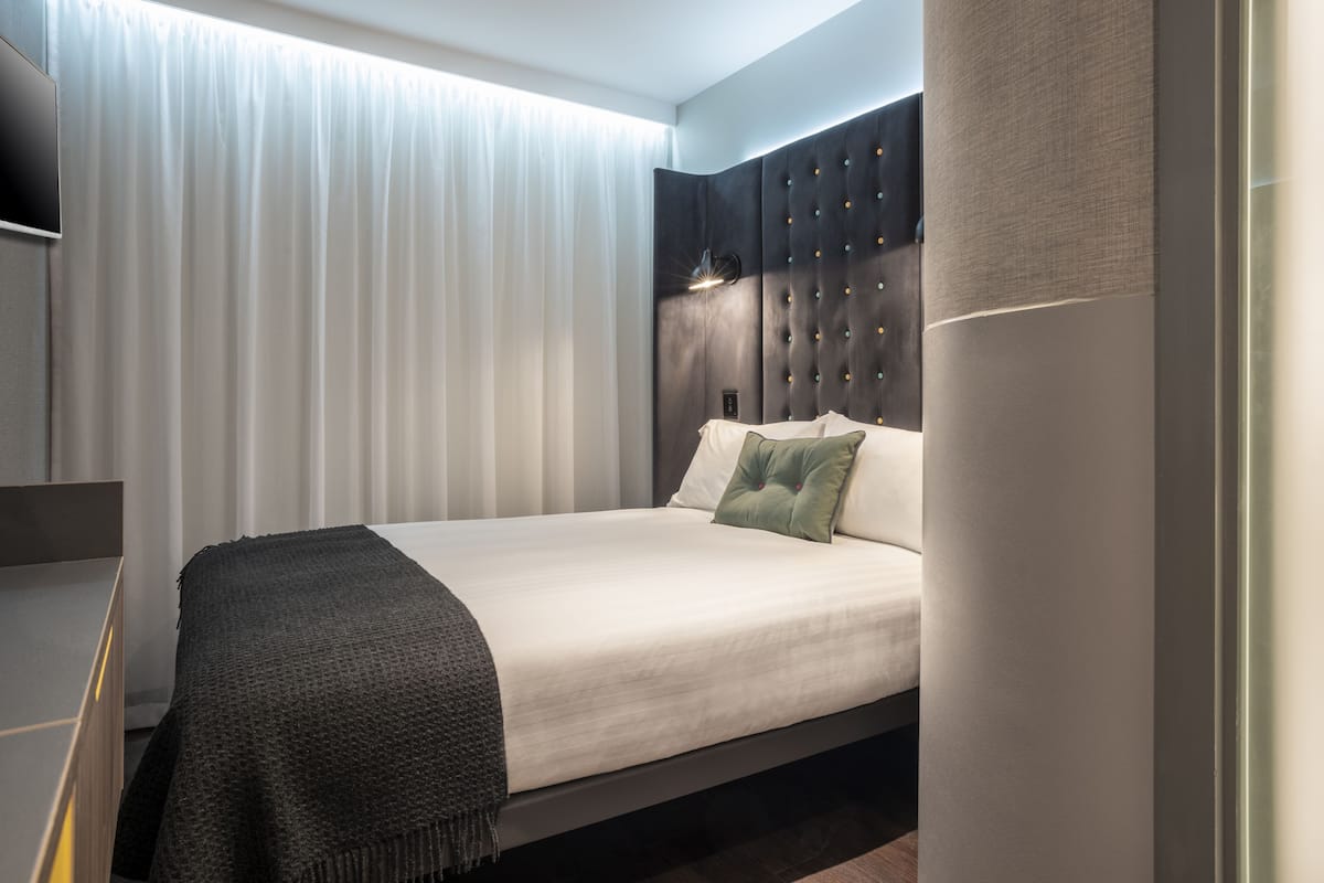Moderni hotellihuone, jossa on sänky, yöpöytä ja suuri ikkuna, jossa on verhot.