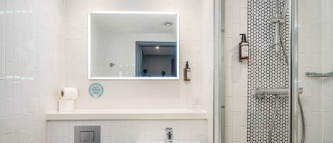 A bathroom with a white sink, a mirror, and a shower with a tiled wall.
