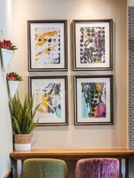 Een muur met vier ingelijste abstracte schilderijen, een potplant en een houten bankje.