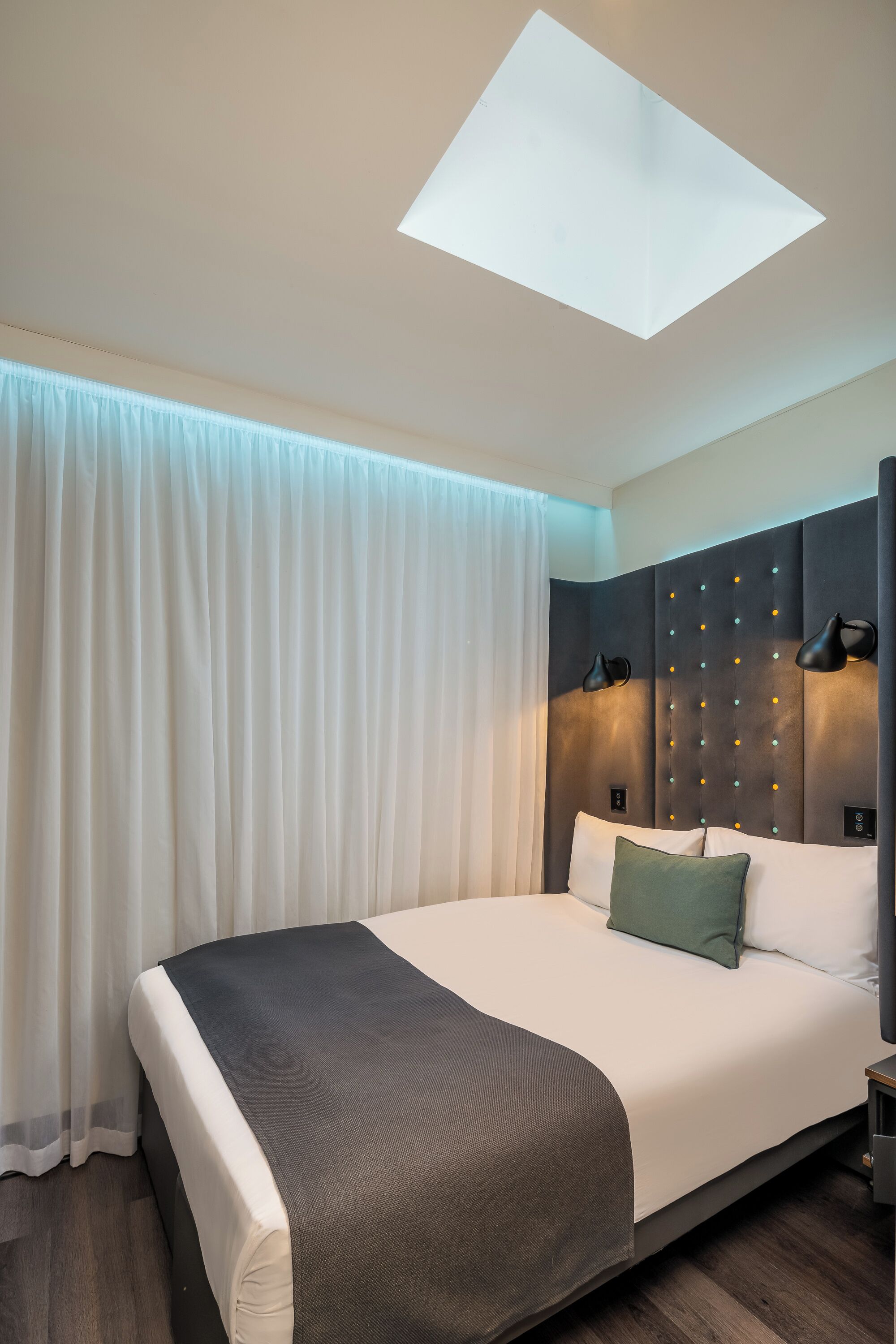 A modern hotel room with a large bed, a ceiling light, and a view of the sky.