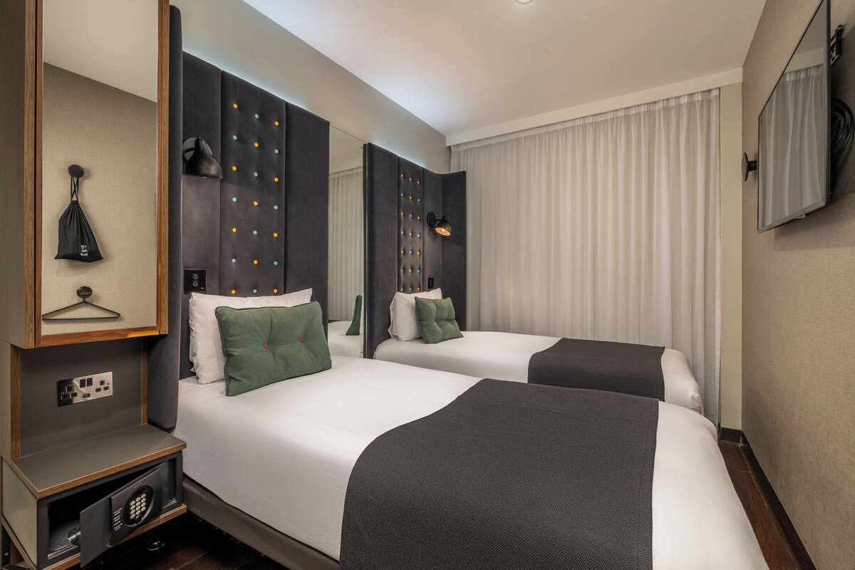 Hotellihuone, jossa on kaksi sänkyä, suuri peili, vaatekaappi ja televisio.
