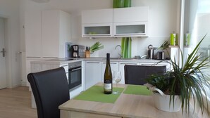 Uma cozinha moderna com armários brancos, uma mesa de jantar com cadeiras, uma cafeteira e uma garrafa de vinho.
