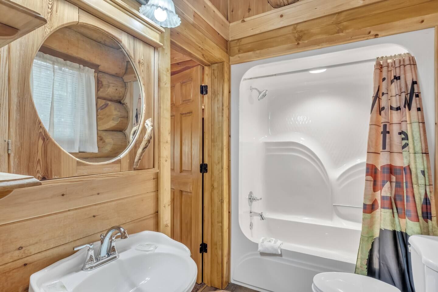 Une salle de bain rustique, avec une cabine en bois, un lavabo, un miroir et une baignoire.