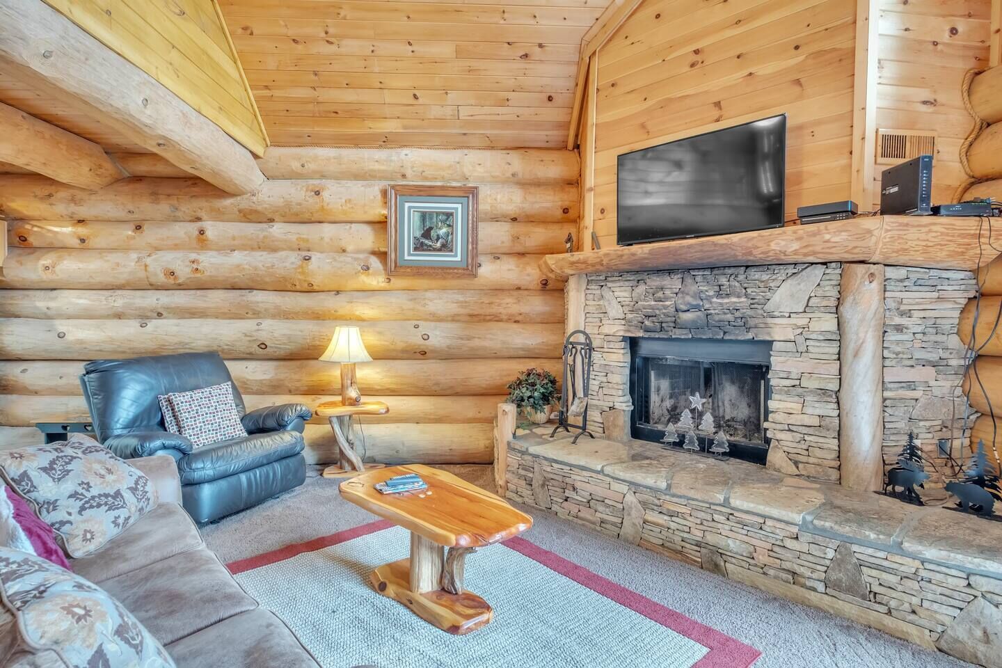 L’intérieur d’une cabane en rondins, avec une cheminée en pierre, un canapé en cuir et un téléviseur fixé au-dessus de la cheminée.