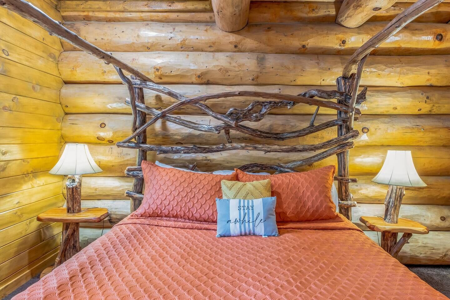 A log cabin bedroom with a bed, pillows, and two bedside lamps.