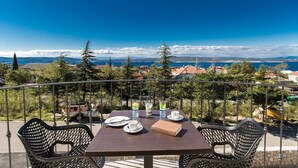 A balcony with a table set for two, overlooking a scenic view of the sea and distant mountains. - Pansion Preza (Crikvenica)