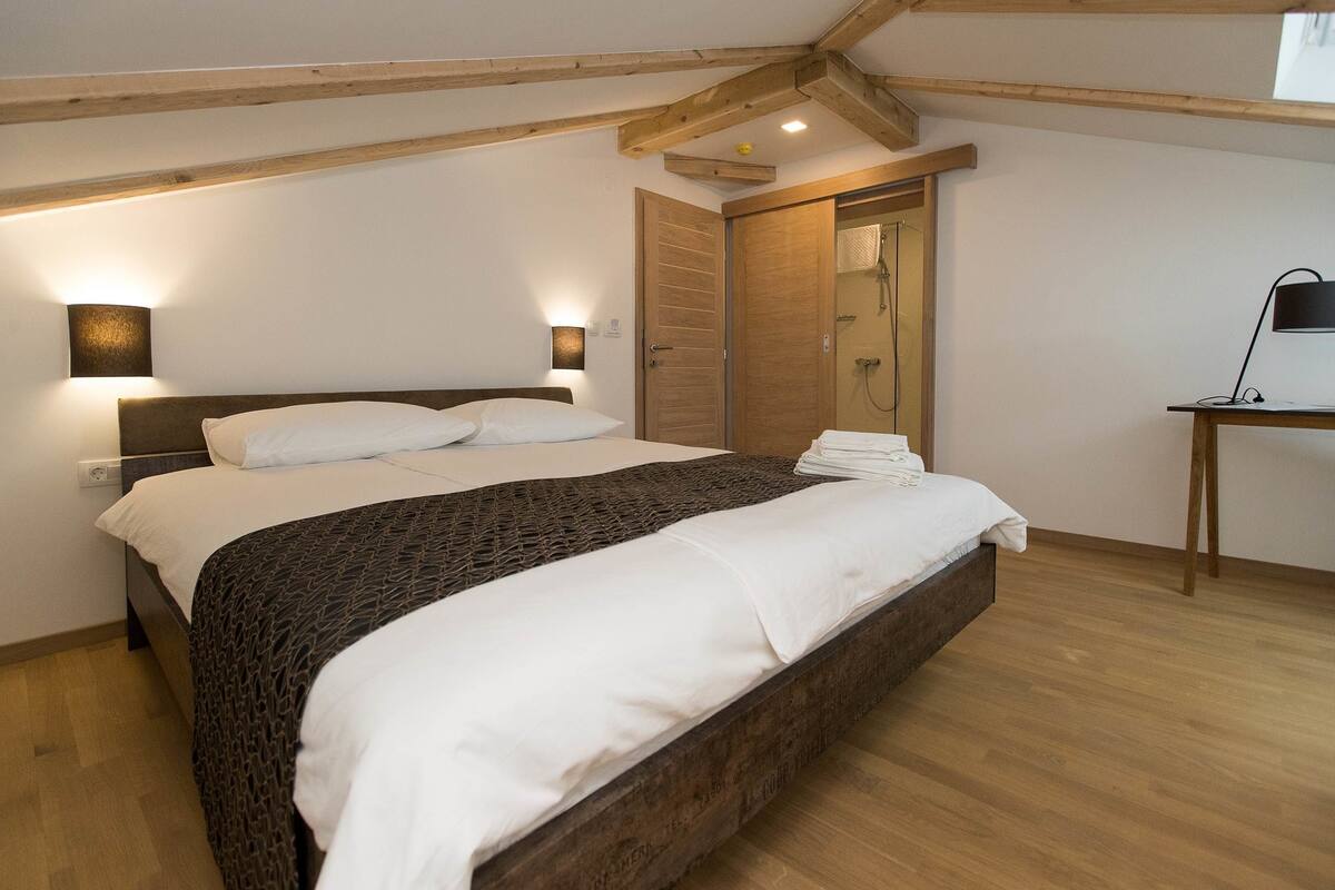 A bedroom with a large bed, wooden beams, a desk, and a wardrobe.