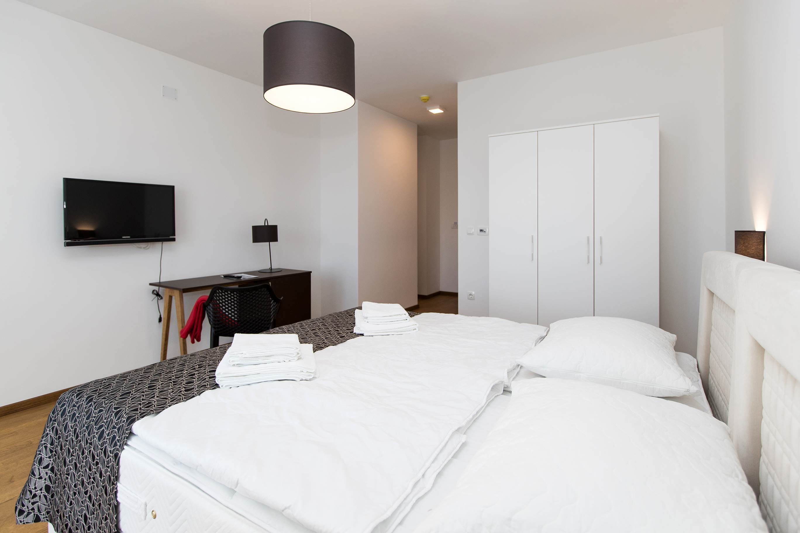 Une chambre d’hôtel moderne avec un lit bien fait, un bureau avec un ordinateur, un téléviseur à écran plat et une armoire.