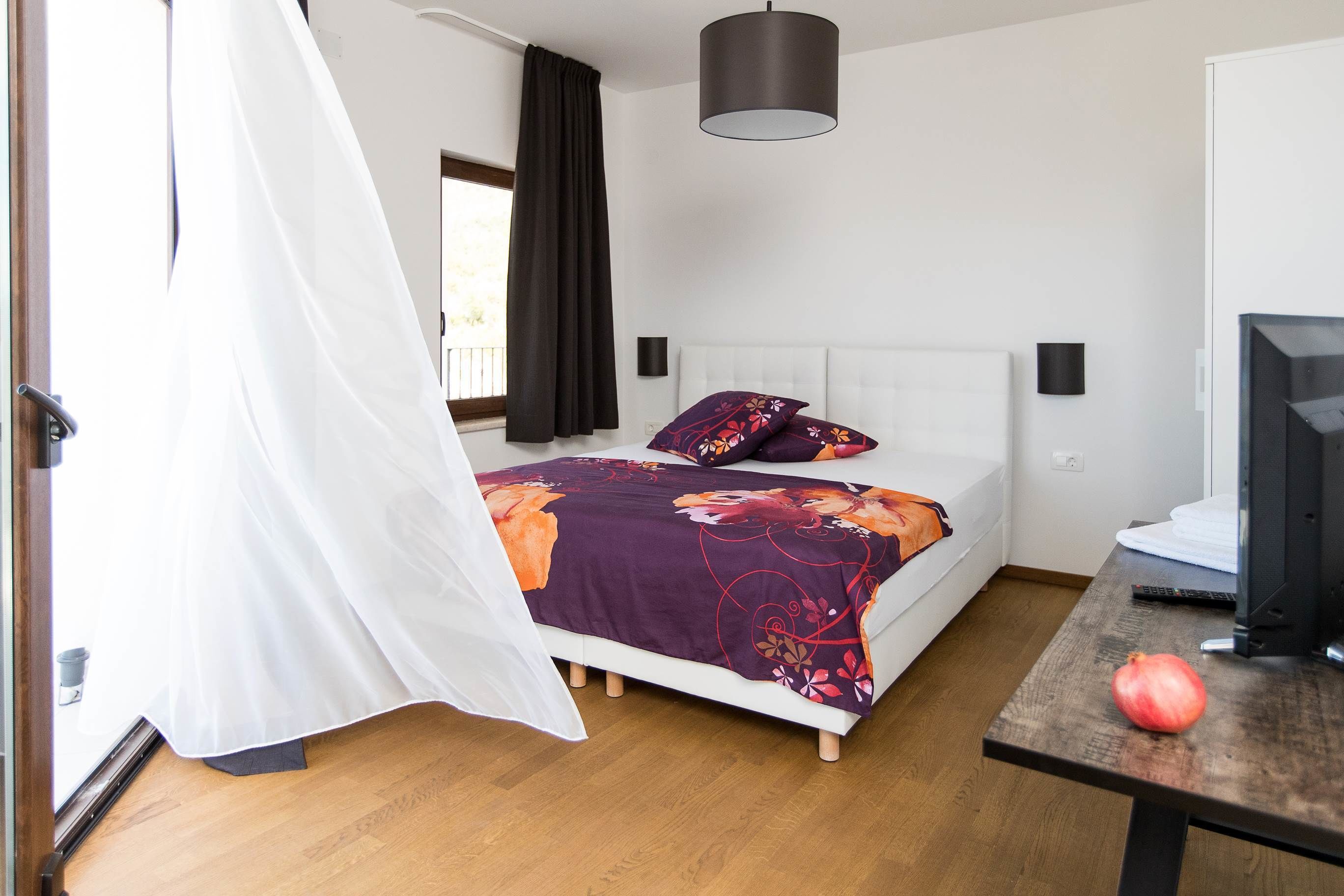 Un dormitorio con cama, televisor, mesa y ventana con cortinas.