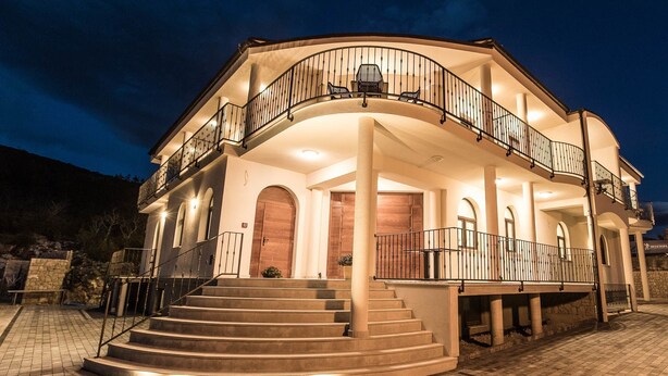 A two-story building with a curved balcony, a staircase leading to the entrance, and a paved driveway. - Pansion Preza (Crikvenica)