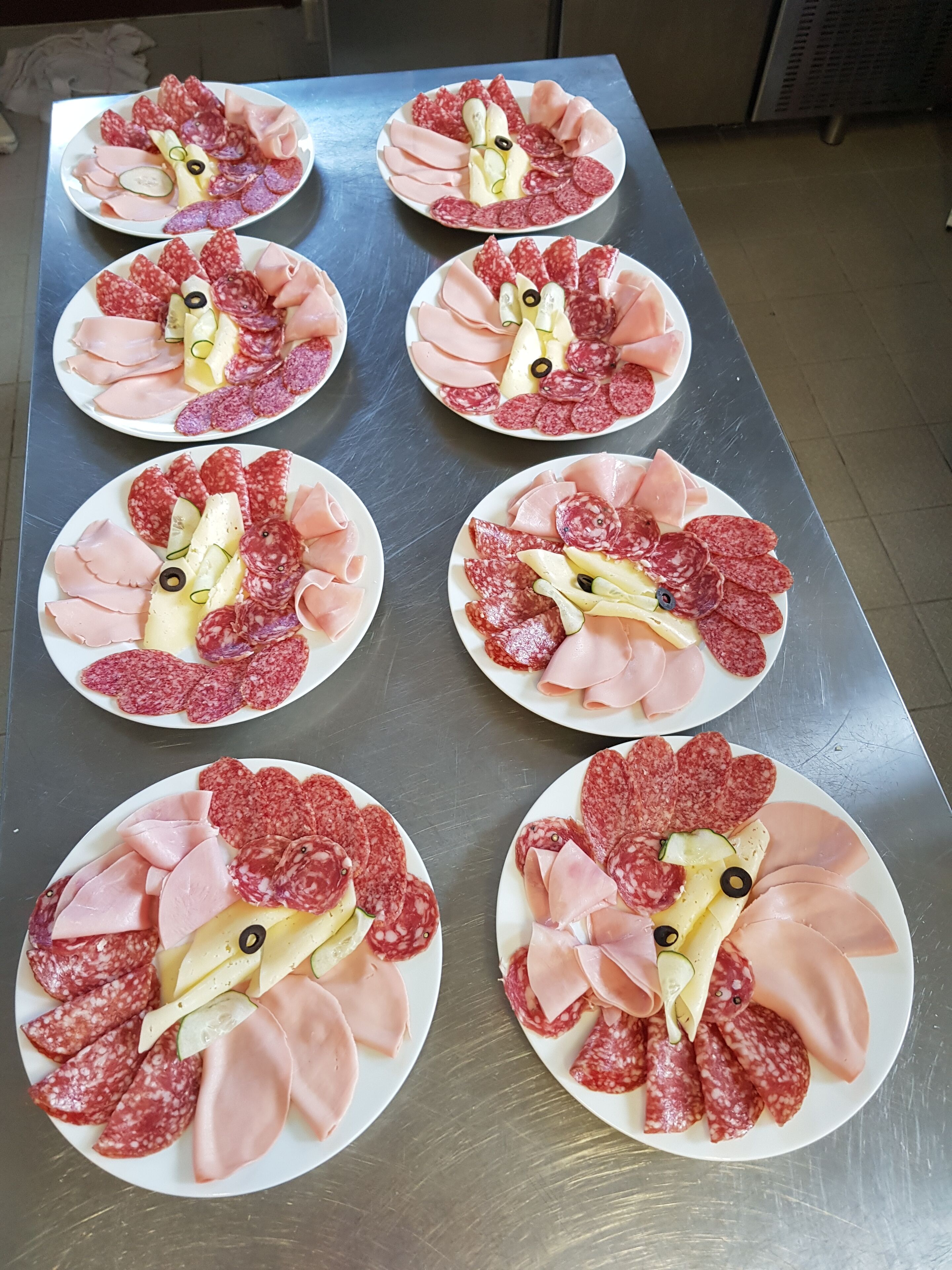 Una mesa de acero inoxidable con seis platos de carnes y quesos variados, dispuestos en un patrón de cuadrícula.